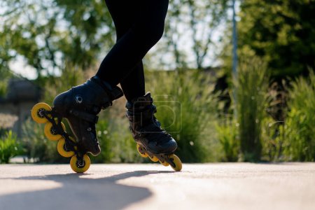 Téléchargez les photos : Fille sportive pratiquant des tours sur patins à roulettes dans le parc sur fond de ville profiter de leçons de patinage à roulettes gros plan roues Concept de sport de rue - en image libre de droit