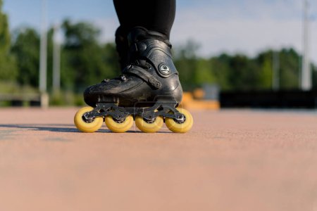 Téléchargez les photos : Fille sportive pratiquant des tours sur patins à roulettes dans le parc sur fond de ville profiter de leçons de patinage à roulettes gros plan roues Concept de sport de rue - en image libre de droit
