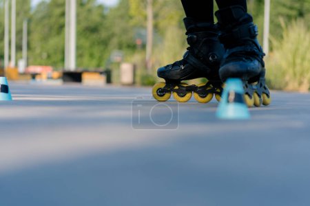 Photo for Sporty girl practicing tricks on roller skates in park on city background enjoying roller skating lesson with chips closeup of street sport - Royalty Free Image