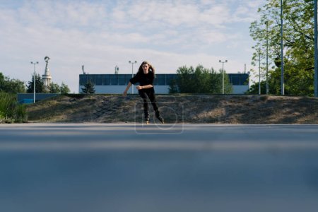 Foto de Chica deportiva paseos patines en el parque en el fondo de la ciudad chica activa en disfruta de patinaje lección calle concepto de deportes de calle - Imagen libre de derechos