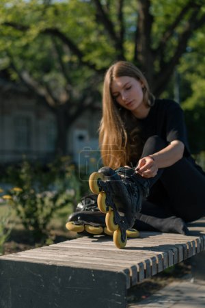 Foto de Joven hermosa chica en parque atando cordones en patín antes de patinar entrenamiento estilo de vida activo hobby - Imagen libre de derechos