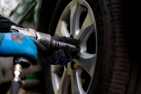 Téléchargez les photos : Mécanicien automobile changer une roue d'une voiture noire à l'aide d'une perceuse dans l'atelier de pneus dans la rue détaillant les réparations de voiture - en image libre de droit