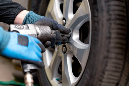 Photo for Auto mechanic changing a wheel from a black car using a drill in tire shop on the street detailing car repairs - Royalty Free Image