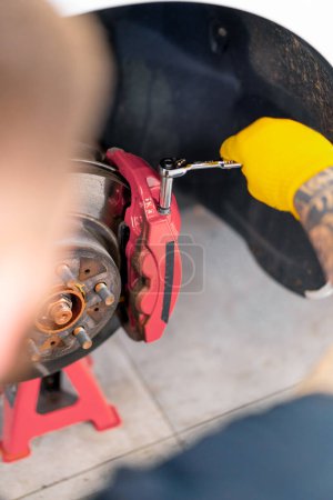 Foto de Hombre mecánico automático cambiando los discos de freno en el coche blanco de lujo usando una llave inglesa en un primer plano de la estación de servicio del coche - Imagen libre de derechos