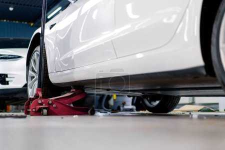 Photo for White luxury car being lifted with a red wheel change jack at car service during detailing and dry cleaning - Royalty Free Image