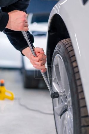 Photo for Auto mechanic man changing a wheel on a luxury white car using balloon wrench at a car service station close-up - Royalty Free Image