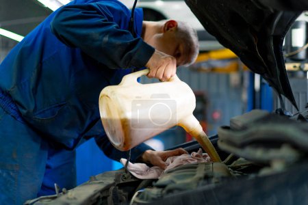 Photo for Male car service worker changing oil in luxury car while undergoing auto maintenance car repairs change of oil - Royalty Free Image