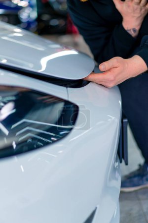 Téléchargez les photos : Un homme souffre en train de se pincer les doigts sous le capot de sa voiture de luxe blanche dans un parking ou un service de voiture en gros plan - en image libre de droit
