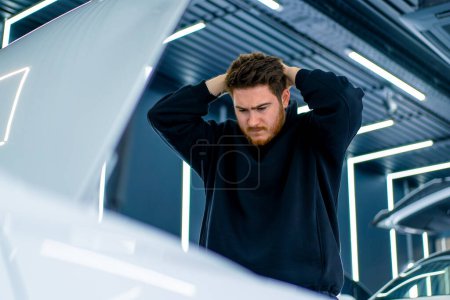 Photo for Portrait of a man shocked by the fact that his white luxury car broke down in a parking lot or at car service - Royalty Free Image