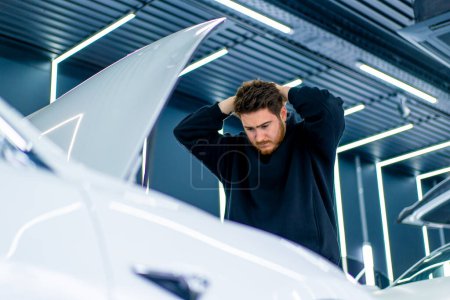 Photo for Portrait of a man shocked by the fact that his white luxury car broke down in a parking lot or at car service - Royalty Free Image
