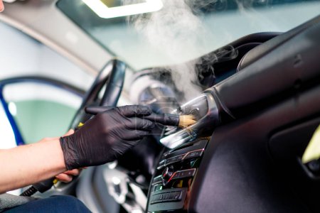 Photo for A car wash worker carefully cleans the interior of a luxury car with a rag a brush vacuum cleaner steamer detailing - Royalty Free Image