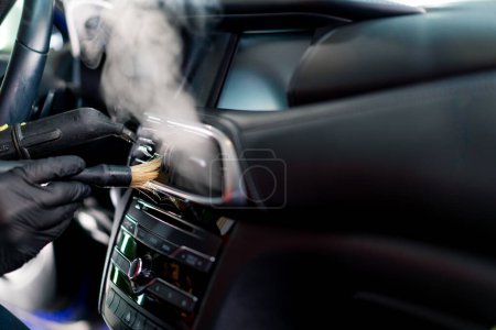 Foto de Un trabajador de lavado de coches limpia cuidadosamente el interior de un coche de lujo con un trapo una aspiradora de cepillo vaporizador detallando - Imagen libre de derechos