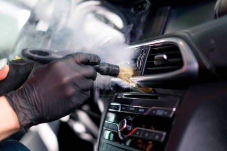 Téléchargez les photos : Un employé de lavage de voiture nettoie soigneusement l'intérieur d'une voiture de luxe avec un chiffon un aspirateur à brosse vapeur détaillant - en image libre de droit