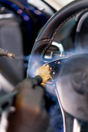 Téléchargez les photos : Un employé de lavage de voiture nettoie soigneusement l'intérieur d'une voiture de luxe avec un chiffon un aspirateur à brosse vapeur détaillant - en image libre de droit