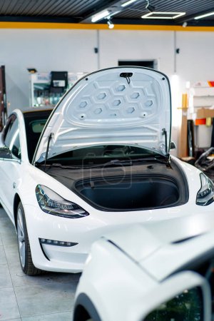Foto de Detallando la capucha abierta y el faro de un coche eléctrico blanco de lujo después de lavar y limpiar en seco en un servicio de automóvil o en el estacionamiento - Imagen libre de derechos