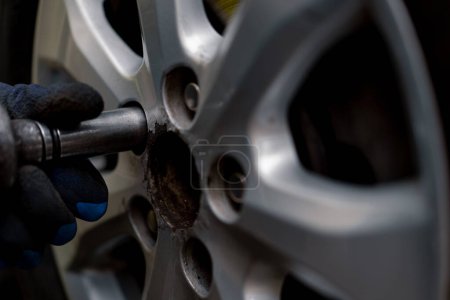 Téléchargez les photos : Gros plan d'un mécanicien qui enlève des gants d'une voiture noire avec une perceuse à l'atelier de réparation de pneus dans la rue détaillant la réparation automobile - en image libre de droit
