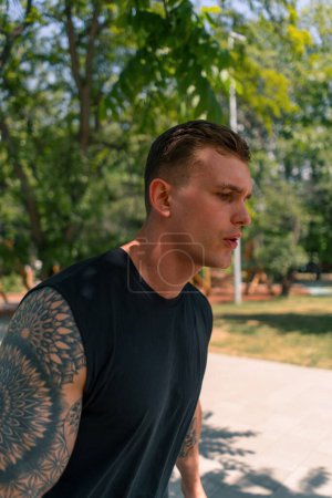 Téléchargez les photos : Portrait jeune coureur tatoué épuisé en tenue de sport courant dans un parc urbain activité sportive de plein air - en image libre de droit