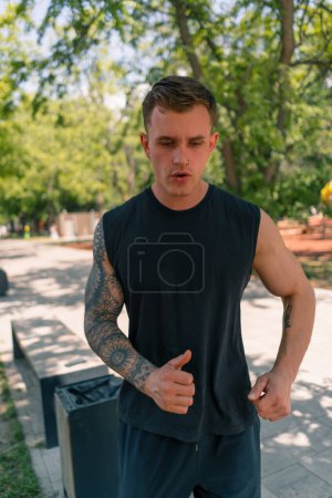 Photo for Portrait young exhausted tattooed runner in sportswear running in urban city park outdoor sports activity - Royalty Free Image