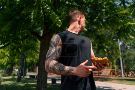 Foto de Joven deportista después de entrenar sosteniendo donas dulces en sus manos duda si comer comida chatarra - Imagen libre de derechos