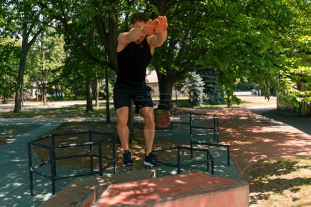 Photo for Young fitness sportsman jumps on a box with both feet, performs a workout at sports street workout - Royalty Free Image