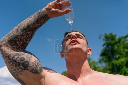 Téléchargez les photos : Jeune bodybuilder sportif debout sur le terrain de sport obtenir éclaboussé de chaleur de l'eau après la formation de rue belle sexy pompé corps - en image libre de droit