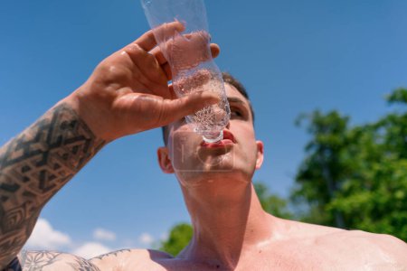 Photo for Young sportsman bodybuilder standing sports field drinking water from bottle after street workout nice sexy pumped up body - Royalty Free Image