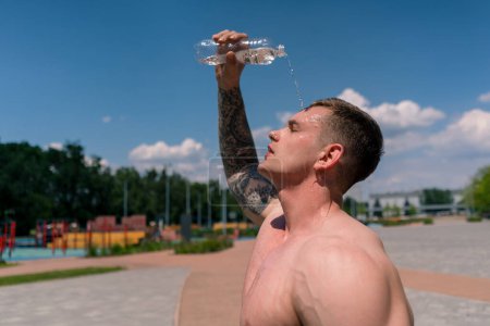 Photo for Young sportsman bodybuilder standing on sports field getting splashed with water heat after street training nice sexy pumped up body - Royalty Free Image