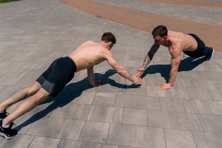 Foto de Entrenador y joven deportista haciendo flexiones en la calle y dándose unos a otros una alta cinco durante los brazos de ejercicio de entrenamiento hombros bonito cuerpo sexy - Imagen libre de derechos
