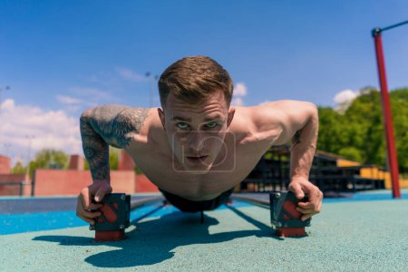 Photo for Young pumped-up athlete doing push-ups from the ground during street training endurance exercise swings arms shoulders - Royalty Free Image