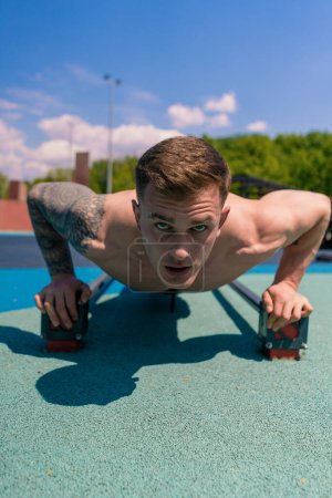 Photo for Young pumped-up athlete doing push-ups from the ground during street training endurance exercise swings arms shoulders - Royalty Free Image