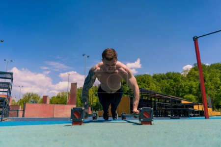 Foto de Joven atleta bombeado haciendo flexiones desde el suelo durante el ejercicio de resistencia de entrenamiento callejero balancea los brazos hombros - Imagen libre de derechos