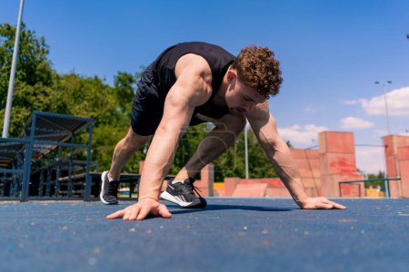 Foto de Joven atleta bombeado haciendo flexiones desde el suelo durante el ejercicio de resistencia de entrenamiento callejero balancea los brazos hombros - Imagen libre de derechos