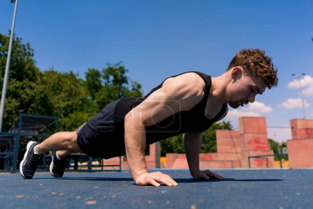 Téléchargez les photos : Jeune athlète pompé faisant des pompes à partir du sol pendant l'entraînement de rue endurance exercice balançoires bras épaules - en image libre de droit