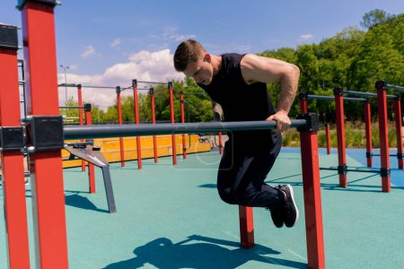 Photo for Portrait of a young sportsman working out on parallel bars swinging his arms and shoulders doing push-ups sports ground during street training - Royalty Free Image