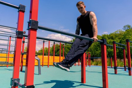 Photo for Portrait of a young sportsman working out on parallel bars swinging his arms and shoulders doing push-ups sports ground during street training - Royalty Free Image