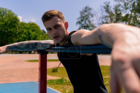 Photo for Portrait of a young sweaty sportsman after an outdoor workout on a horizontal bar parallel bars - Royalty Free Image