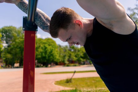 Téléchargez les photos : Portrait d'un jeune sportif en sueur après une séance d'entraînement en plein air sur une barre horizontale barres parallèles - en image libre de droit