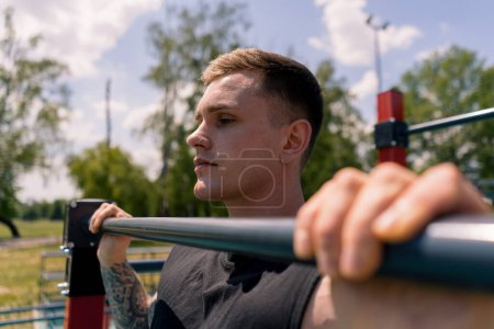Photo for Portrait of a young sweaty sportsman doing horizontal bar swings arms and shoulders push-ups sports ground during street training - Royalty Free Image