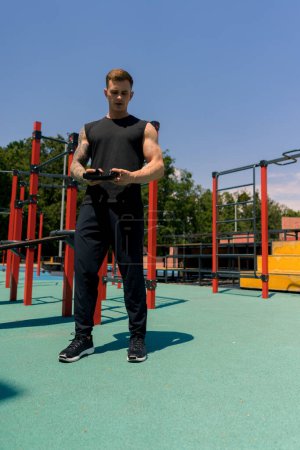 Téléchargez les photos : Portrait d'un jeune sportif en sueur avec tatouages et piercings tenant des écouteurs sur le terrain de sport entraînement en plein air dans la motivation du parc - en image libre de droit