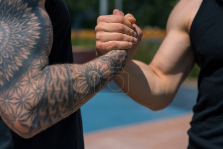 Photo for Personal fitness trainer or bodybuilder and young sportsman shaking hands before starting competition on sports ground close-up tattooed hands - Royalty Free Image