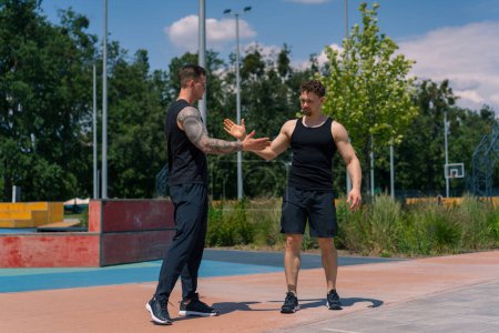 Foto de Entrenador de fitness personal y joven deportista se saludan en el campo de deportes Dos chicos activos antes de comenzar el entrenamiento - Imagen libre de derechos