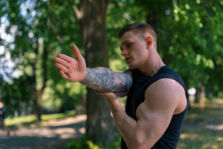 Photo for Portrait of a young sportsman with tattoos doing warm-up exercises outdoors street training in park motivation - Royalty Free Image
