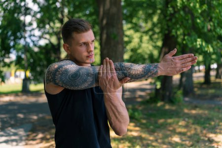 Photo for Portrait of a young sportsman with tattoos doing warm-up exercises outdoors street training in park motivation - Royalty Free Image
