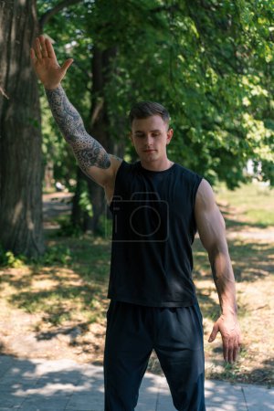 Foto de Retrato de un joven deportista con tatuajes haciendo ejercicios de calentamiento al aire libre entrenamiento callejero en la motivación del parque - Imagen libre de derechos