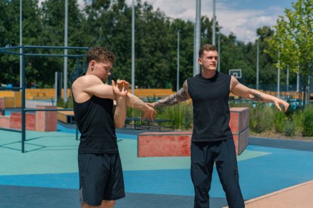 Photo for Personal fitness trainer training athlete on sports ground Two active guys training outdoors doing warmup before exercise - Royalty Free Image