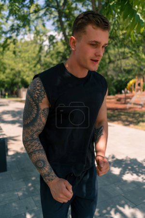 Foto de Retrato joven agotado corredor tatuado en ropa deportiva corriendo en el parque urbano de la ciudad actividad deportiva al aire libre - Imagen libre de derechos