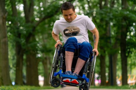 Téléchargez les photos : Inclusivité Un homme handicapé fait des cascades en fauteuil roulant dans un parc municipal sur fond d'arbres - en image libre de droit