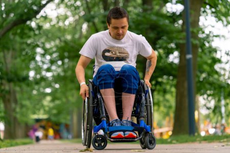 Photo for Inclusiveness A man with disabilities rides a wheelchair along the path of city park against the background of trees - Royalty Free Image
