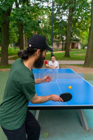 Téléchargez les photos : Inclusivité vieil homme jouant au ping-pong contre un homme handicapé qui est en fauteuil roulant dans un parc municipal - en image libre de droit