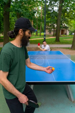 Photo for Inclusiveness  old man playing ping-pong against a man with disabilities who is in a wheelchair in city park - Royalty Free Image